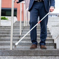 Blind person uses cane to descend stairs